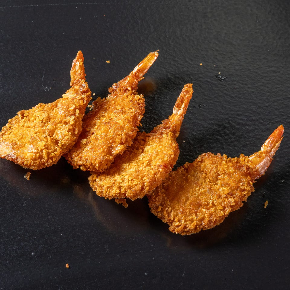 Four golden-brown breaded shrimp arranged on a black slate surface.