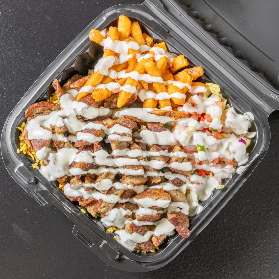 Takeout container filled with seasoned rice, sliced grilled meat, fries, salad, and creamy white sauce.