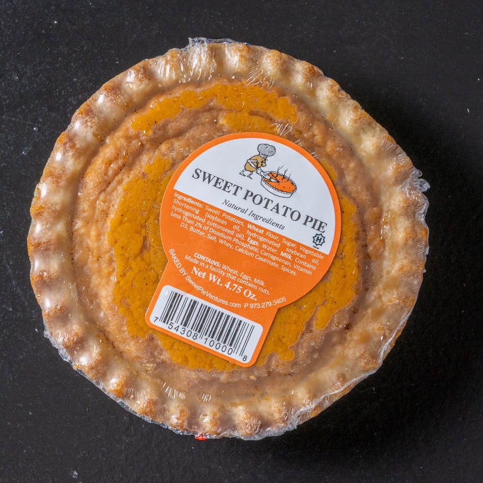 Packaged sweet potato pie with a crimped crust and orange label, photographed on a dark surface.