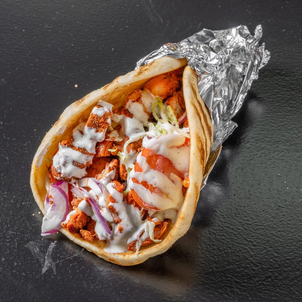 Gyro pita filled with seasoned meat, lettuce, tomatoes, red onions, and creamy white sauce, partially wrapped in foil.