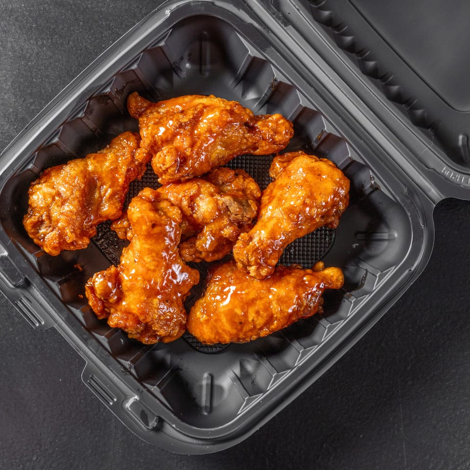 Open black takeout container filled with crispy fried chicken pieces coated in glossy orange sauce.