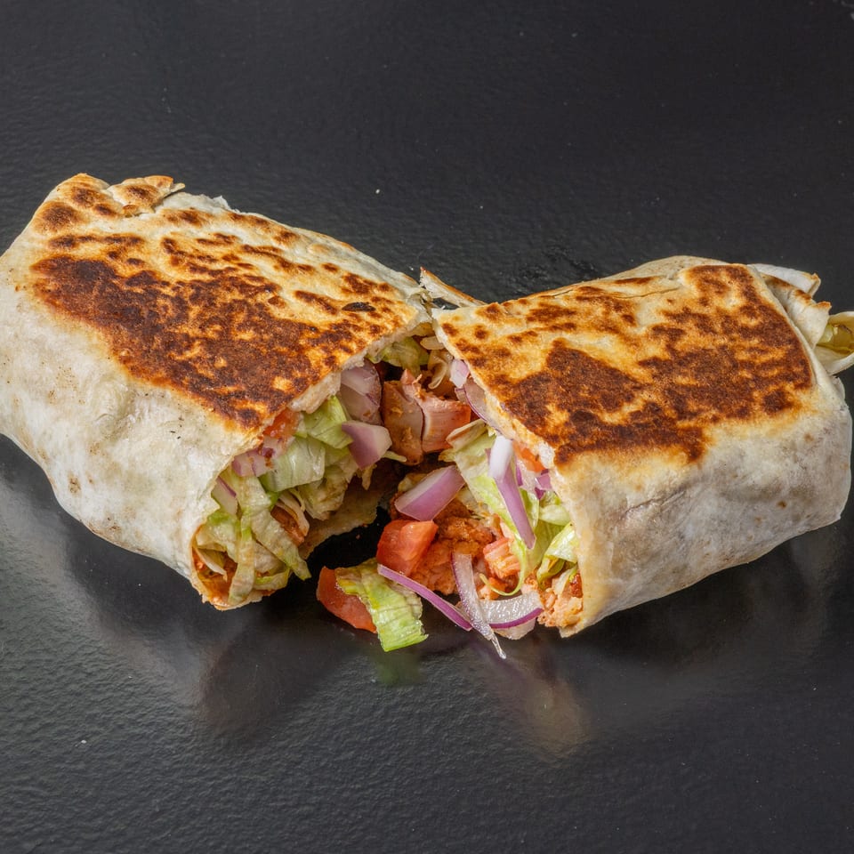 Two toasted flatbread wraps filled with seasoned meat, lettuce, tomatoes, and red onions on a black surface.