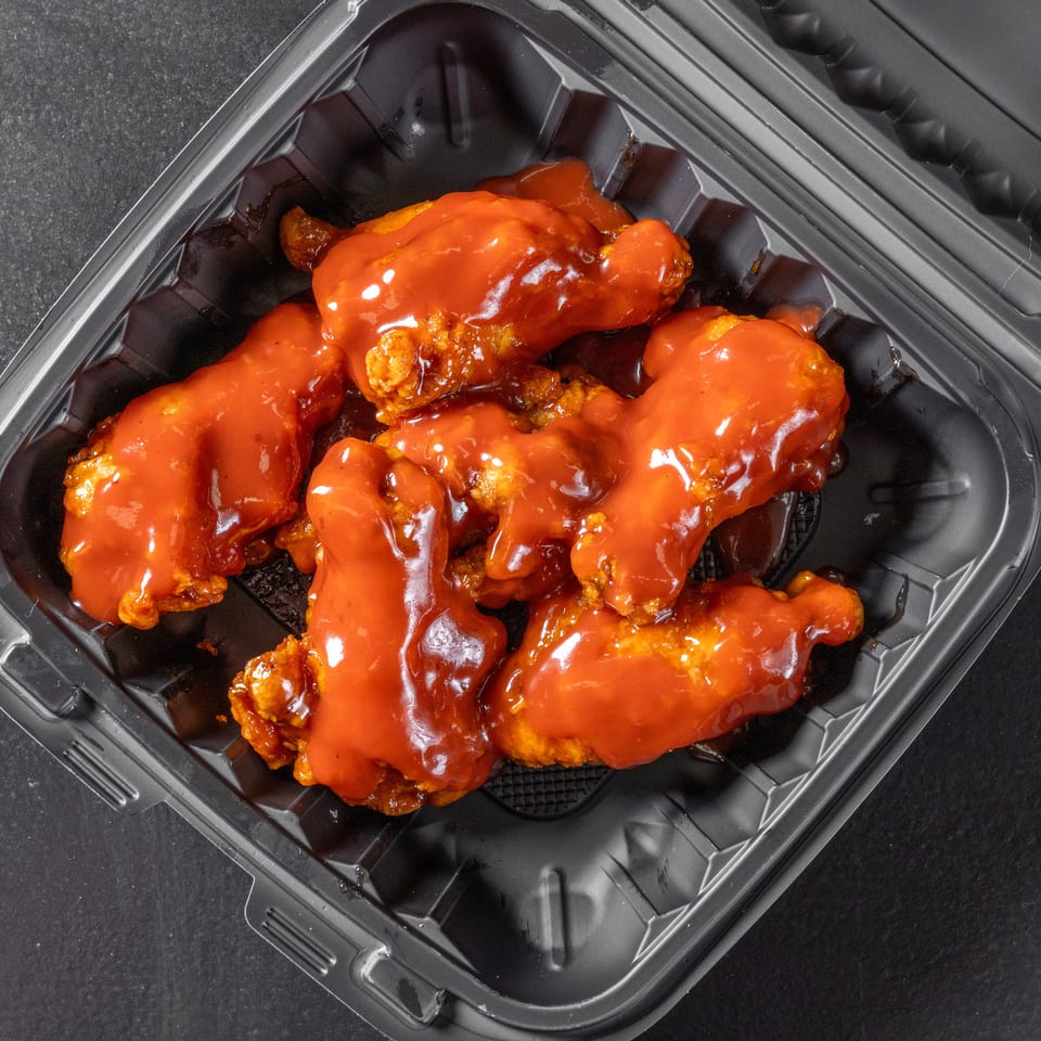 Crispy chicken wings coated in glossy red sauce, arranged in a black takeout container.