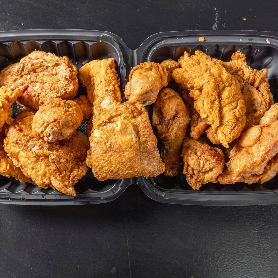 Two black trays filled with assorted golden-brown pieces of crispy fried chicken on a dark surface.