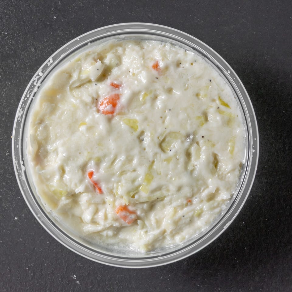 Creamy vegetable dish with carrots and celery served in a clear bowl on a dark countertop.