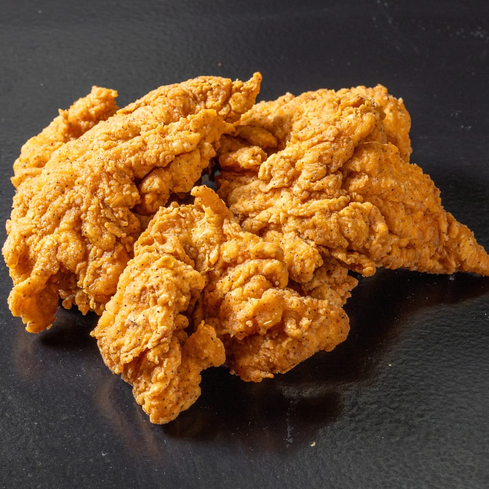 Pile of golden-brown crispy fried chicken tenders on a dark surface.