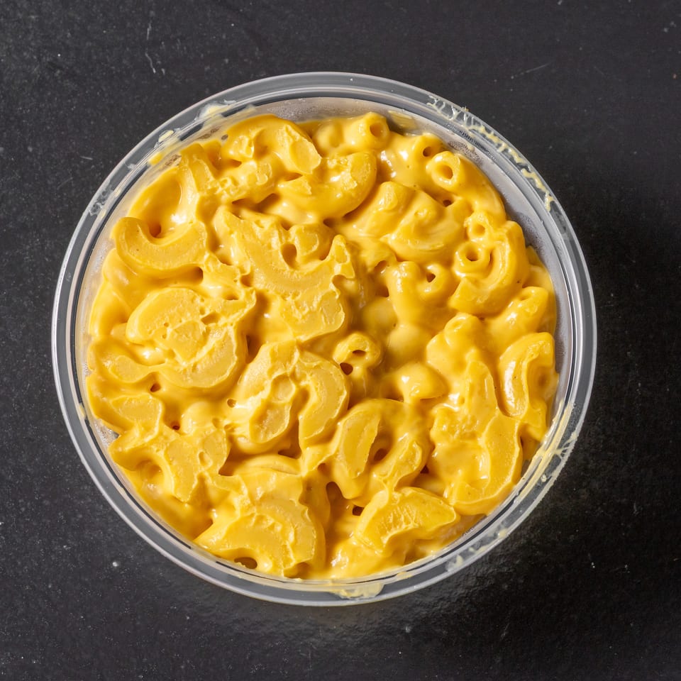 Overhead view of creamy macaroni and cheese in a clear bowl on a dark countertop.