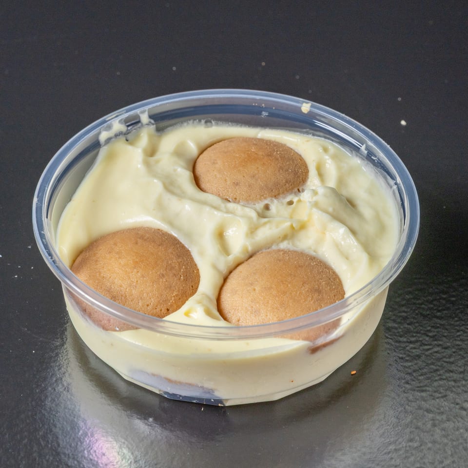 Clear container of creamy vanilla pudding layered with round golden cookies on a dark tabletop.