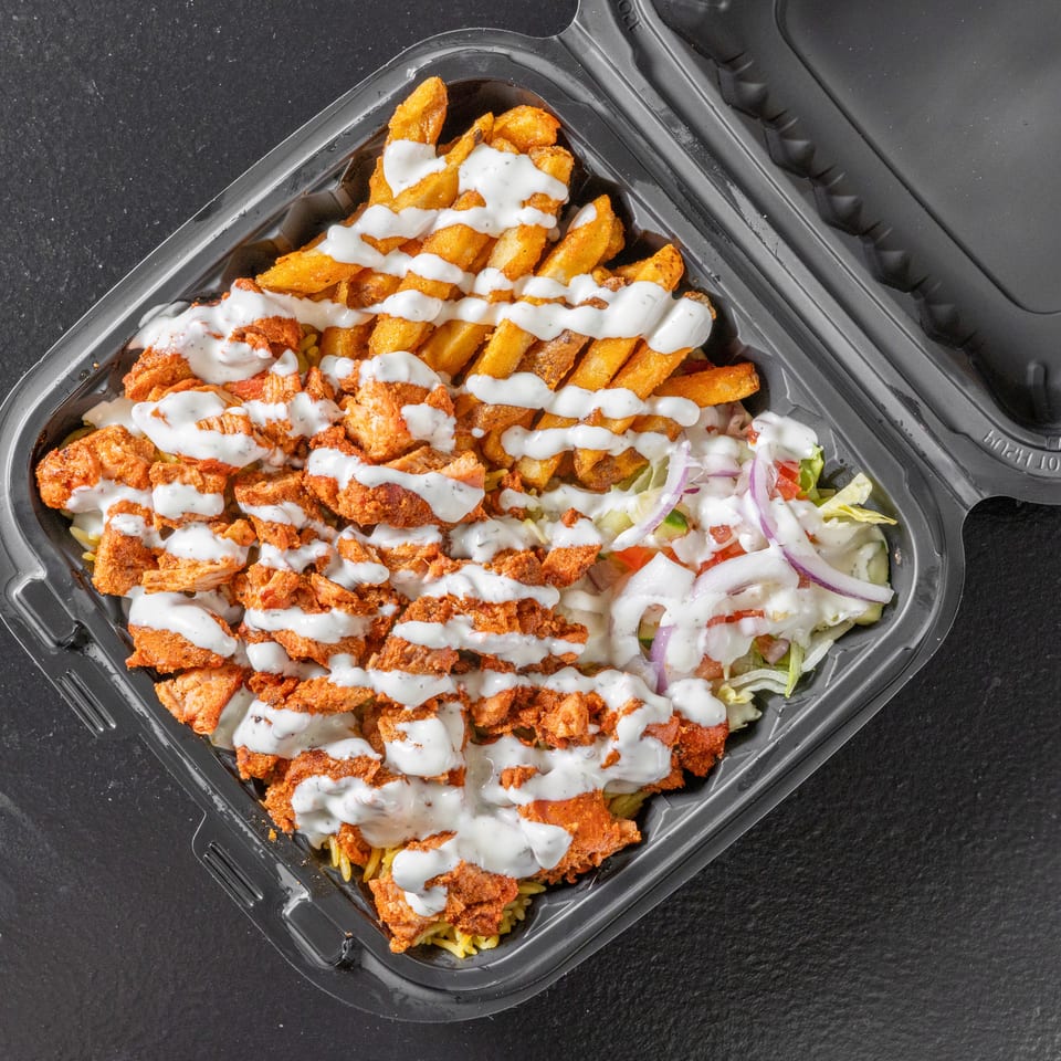 Takeout container filled with seasoned chicken, fries, salad, rice, and creamy white sauce.