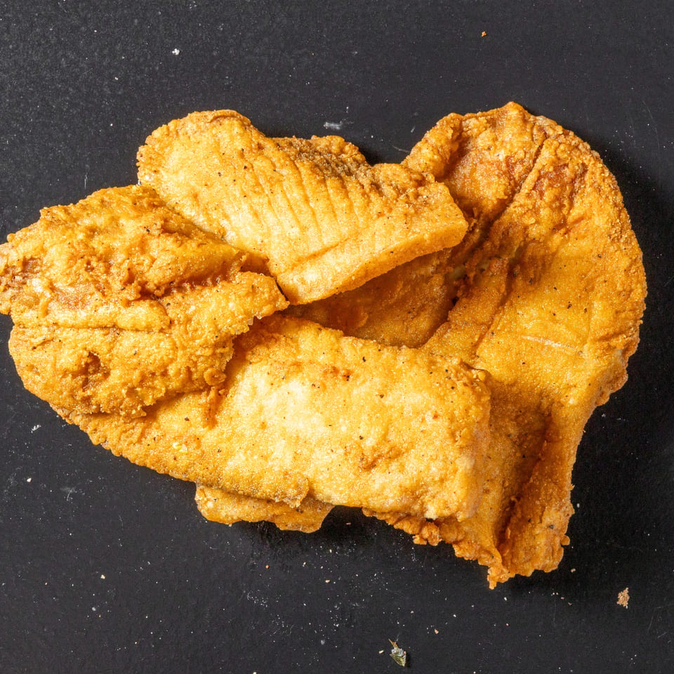 Pile of golden-brown crispy fried chicken pieces arranged on a dark surface.
