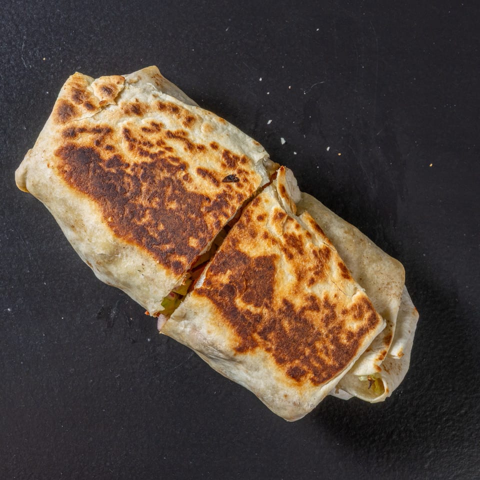 Two grilled, folded flatbread sandwiches with browned, crispy surfaces on a black slate background.