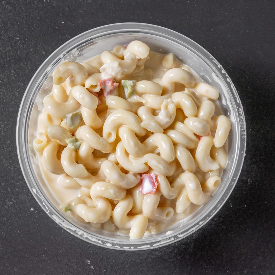 Creamy macaroni salad with diced vegetables in a clear bowl on a dark countertop.