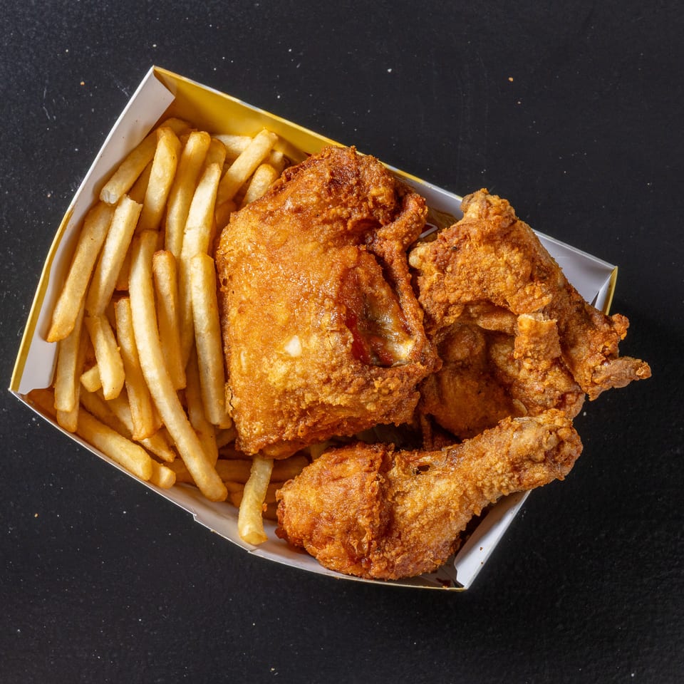 Basket of crispy fried chicken pieces and golden french fries on a black tabletop.
