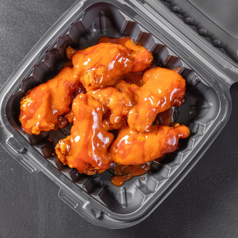Crispy chicken wings coated in glossy orange sauce inside a black takeout container.